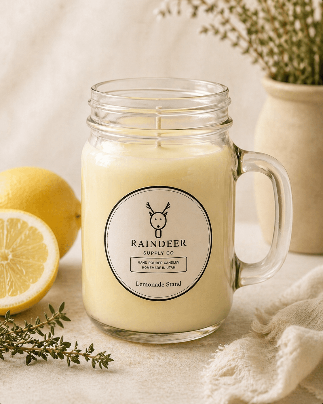 Raindeer Supply Co Lemonade Stand candle in a clear mason jar, surrounded by fresh lemons, thyme, and a draped linen cloth — small-batch hand-poured in Utah.